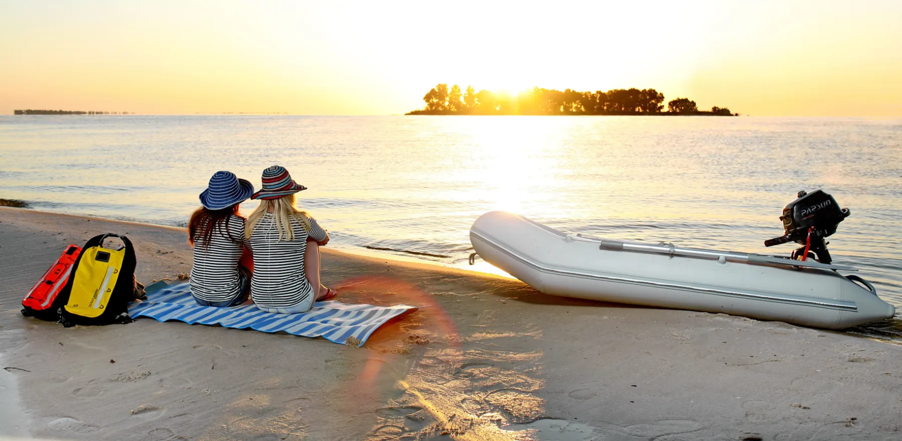 A white inflatable tender with a Parsun outboard pulled up on a beach at sunset